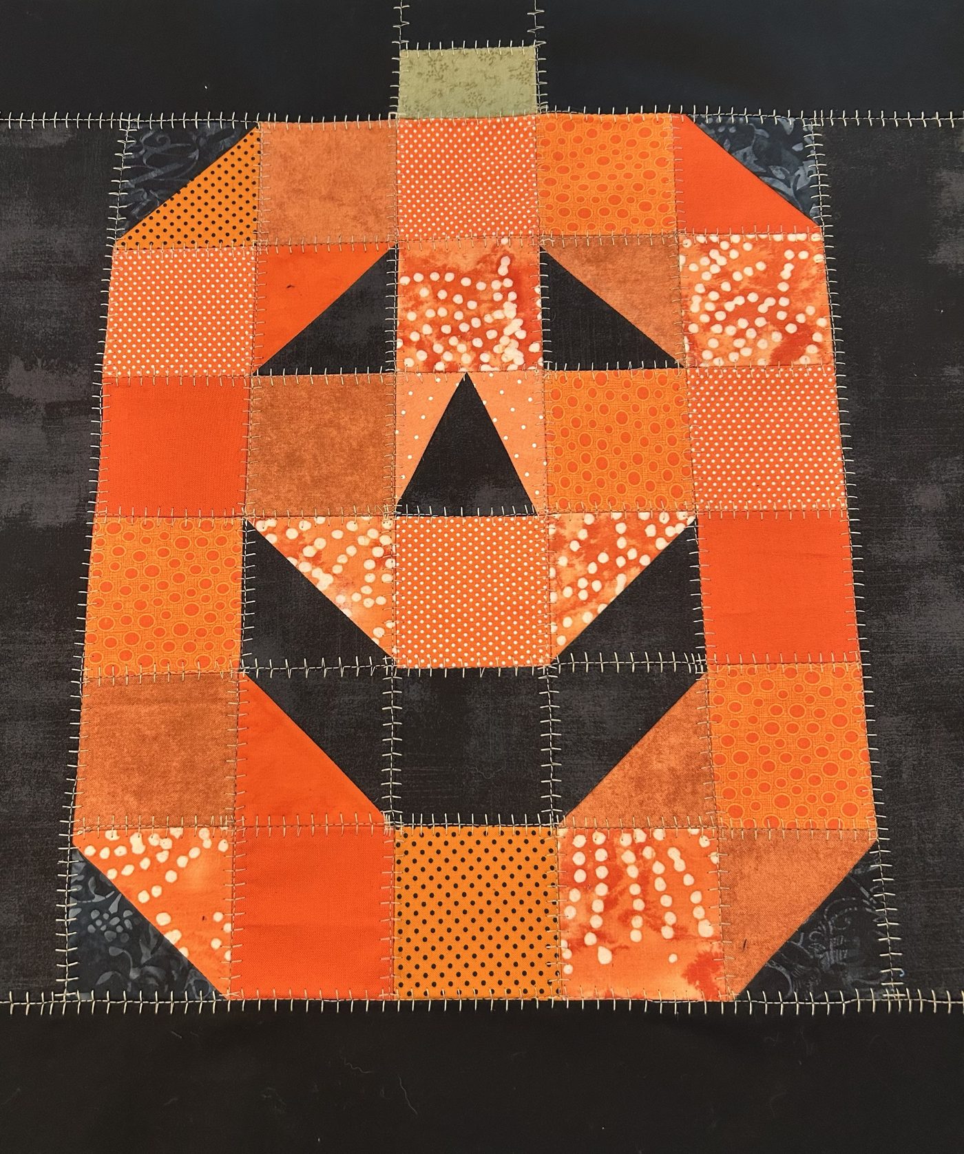 A jack-o'-lantern quilt block pieced from orange prints on black, finished with a hand blanket stitch