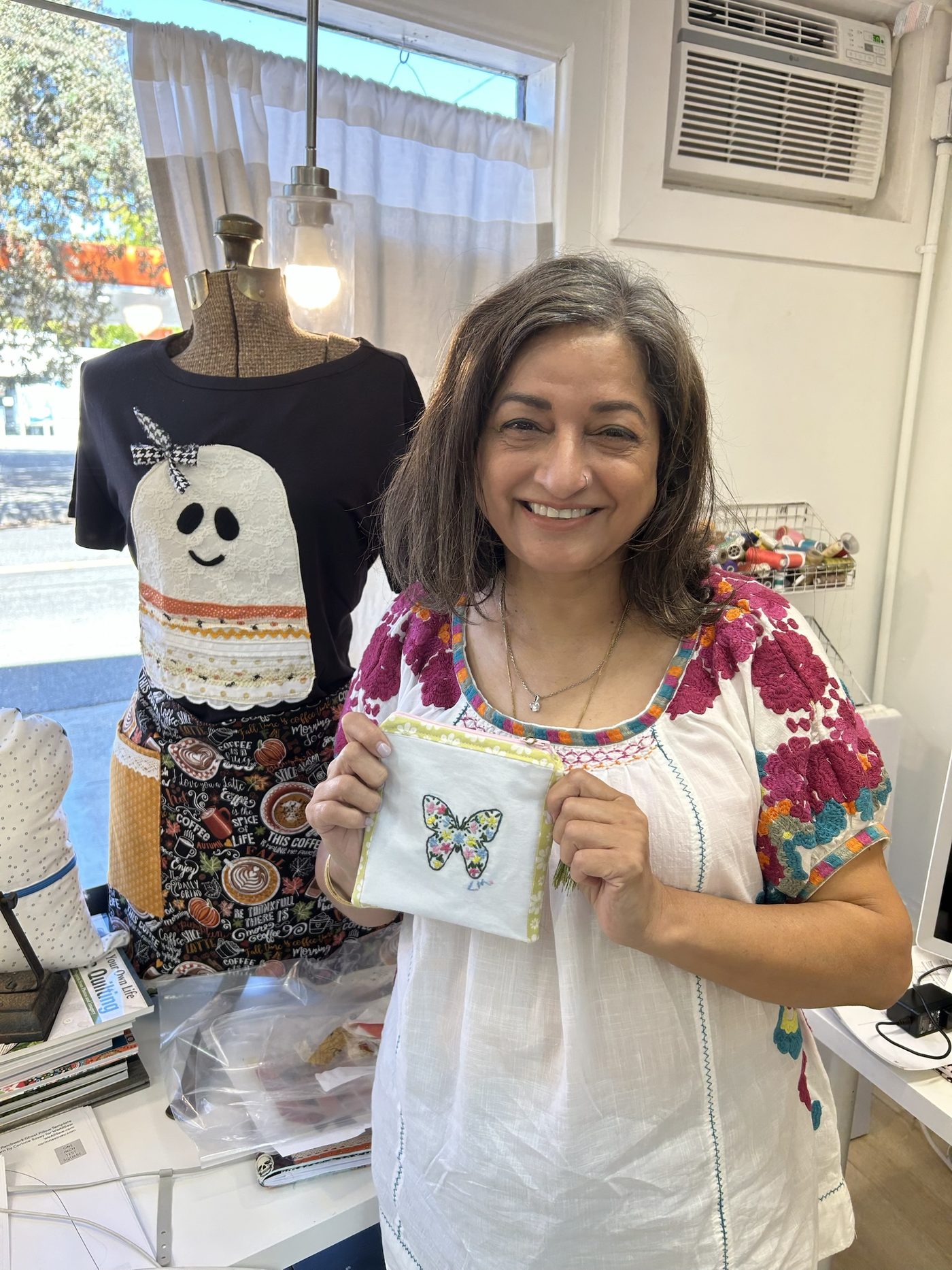 A student in the studio holding the embroidered butterfly zip pouch she finished